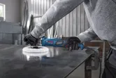 一名佩戴安全設備的人正在用藍色電動工具拋光金屬板。.