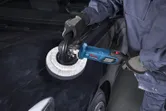 一名佩戴安全設備的人正在使用拋光機拋光黑色汽車引擎蓋。.