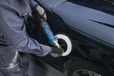 一名配戴安全設備的人員正在使用電動拋光機拋光車門。.