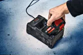 一個人將無線工具電池插入水泥地面上的充電站。.