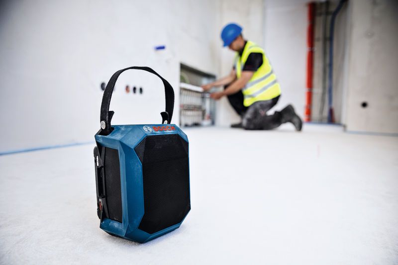 建築工地地板上的藍牙揚聲器，背景的人穿著安全設備。.