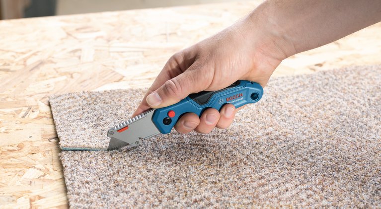 有人在木質表面上用美工刀切割地毯。