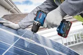 一名穿戴安全裝備的人員使用無線電鑽將支架固定在太陽能板上。