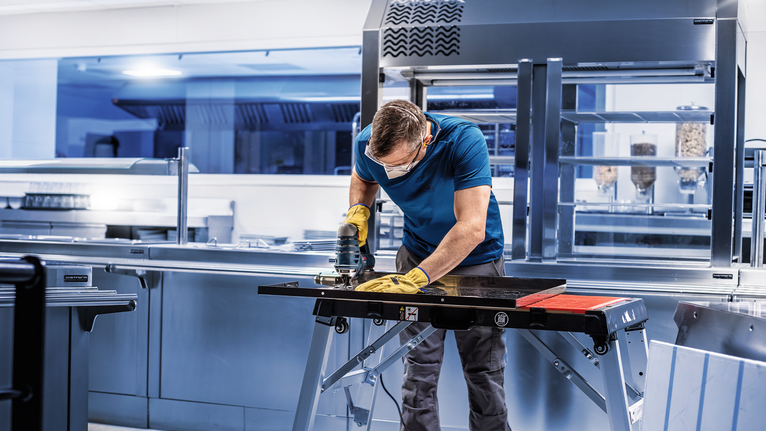 配戴安全設備的人員使用電動工具在商業廚房中切割金屬。.