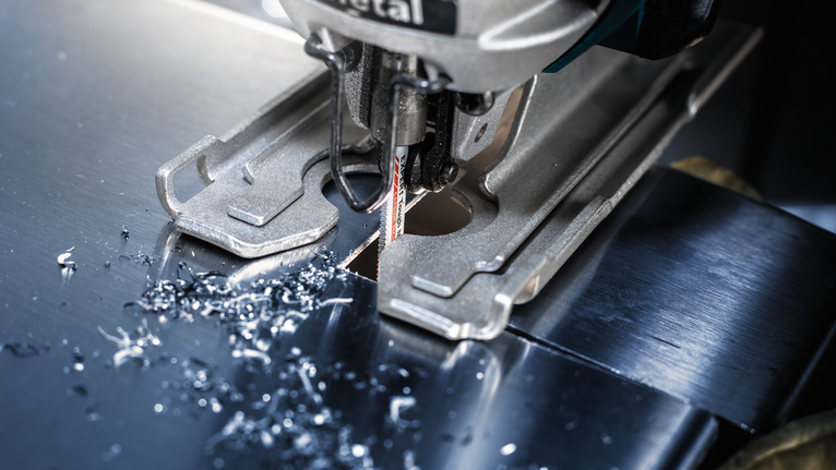 拼圖鋸切割一塊金屬板，小金屬屑散落在刀片周圍。.