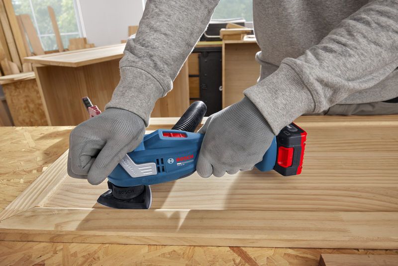 A person wearing safety equipment sands a wooden frame with a multifunction tool.