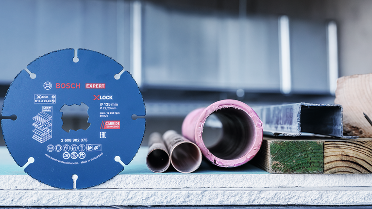 超耐久鎢鋼多功能切片 X-LOCK 切削砂輪片 125 mm,22.23 mm 圓鋸片直立在金屬管道和建築材料旁。