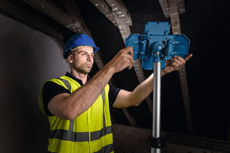 一名穿戴安全裝備的工人正在調整支架上的無線工地照明燈。