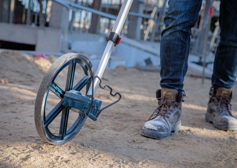 一名穿著工作靴的工人在沙質建築工地上使用測量輪。