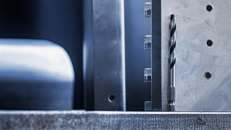 金屬鑽頭垂直對準加工過的金屬表面，該表面已鑽孔。