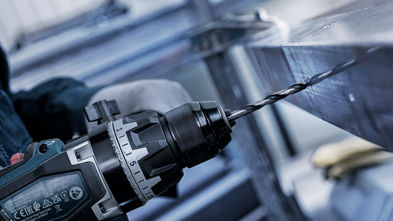 一名穿戴安全裝備的人員在金屬樑上鑽孔。