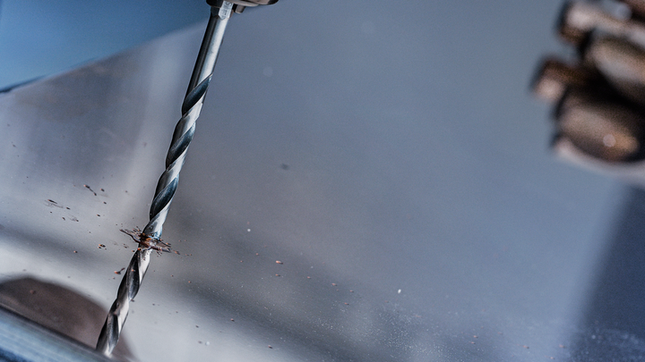 一名穿著安全裝備的人員正在金屬板上鑽孔。