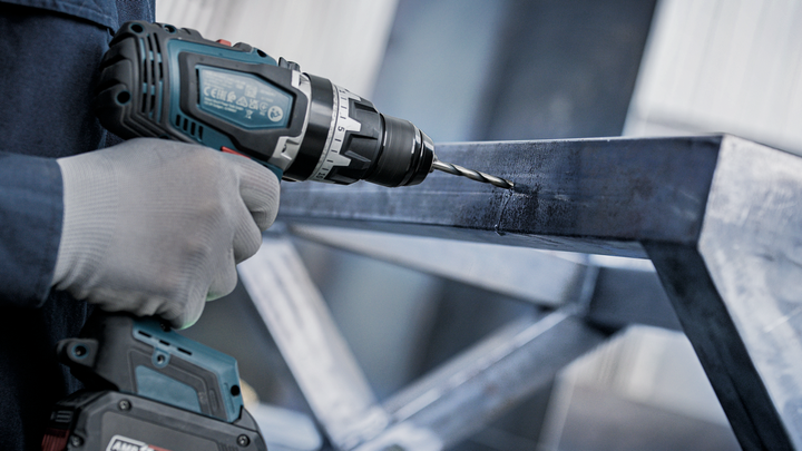 一名穿戴安全裝備的人員正在金屬框架上鑽孔。