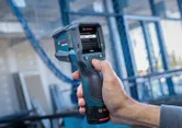 Person operating a thermo detector with a digital display at a construction site.