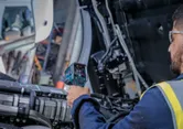 A person wearing safety equipment checks engine temperature with a thermo detector.