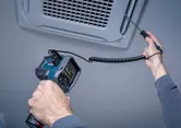 A person uses a thermo detector to measure temperature at an air vent.