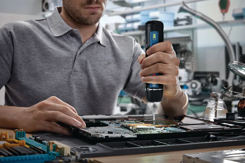 Person using a cordless screwdriver to assemble electronic components on a circuit board.
