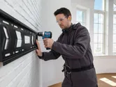 一名配戴安全裝備的人員使用無線電鑽安裝牆壁支架。