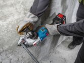 A person wearing safety equipment uses a cordless tool to cut rebar next to a concrete wall.