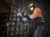 A worker wearing safety equipment cuts rebar on a construction site using a cordless rebar cutter.