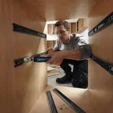 A person wearing safety equipment uses a cordless screwdriver to install drawer slides.