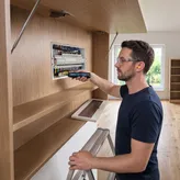 A person wearing safety equipment uses a cordless screwdriver on an electrical panel.