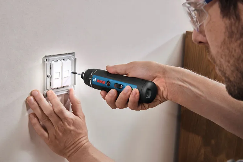 Person wearing safety equipment uses a cordless screwdriver to install a wall switch.