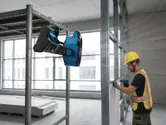 一名配戴安全裝備的人員在固定式便攜式風扇附近操作電動工具。