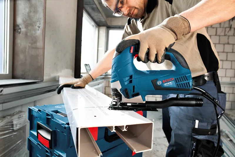A person wearing safety equipment uses a jigsaw to cut a plastic channel.